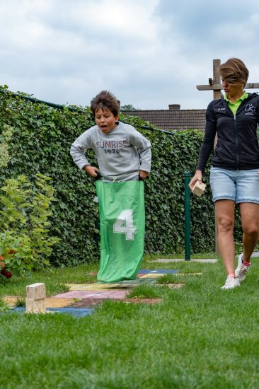 Kind doet psychomotorische therapie in een zak tijdens een buitenactiviteit, begeleid door een therapeute op het gras.